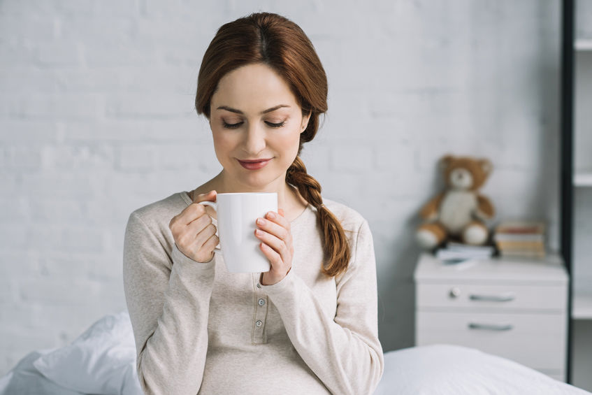 beautiful pregnant woman holding cup of tea in bedroom